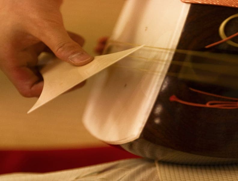 Close-up of an ivory plectrum striking the strings of a shamisen