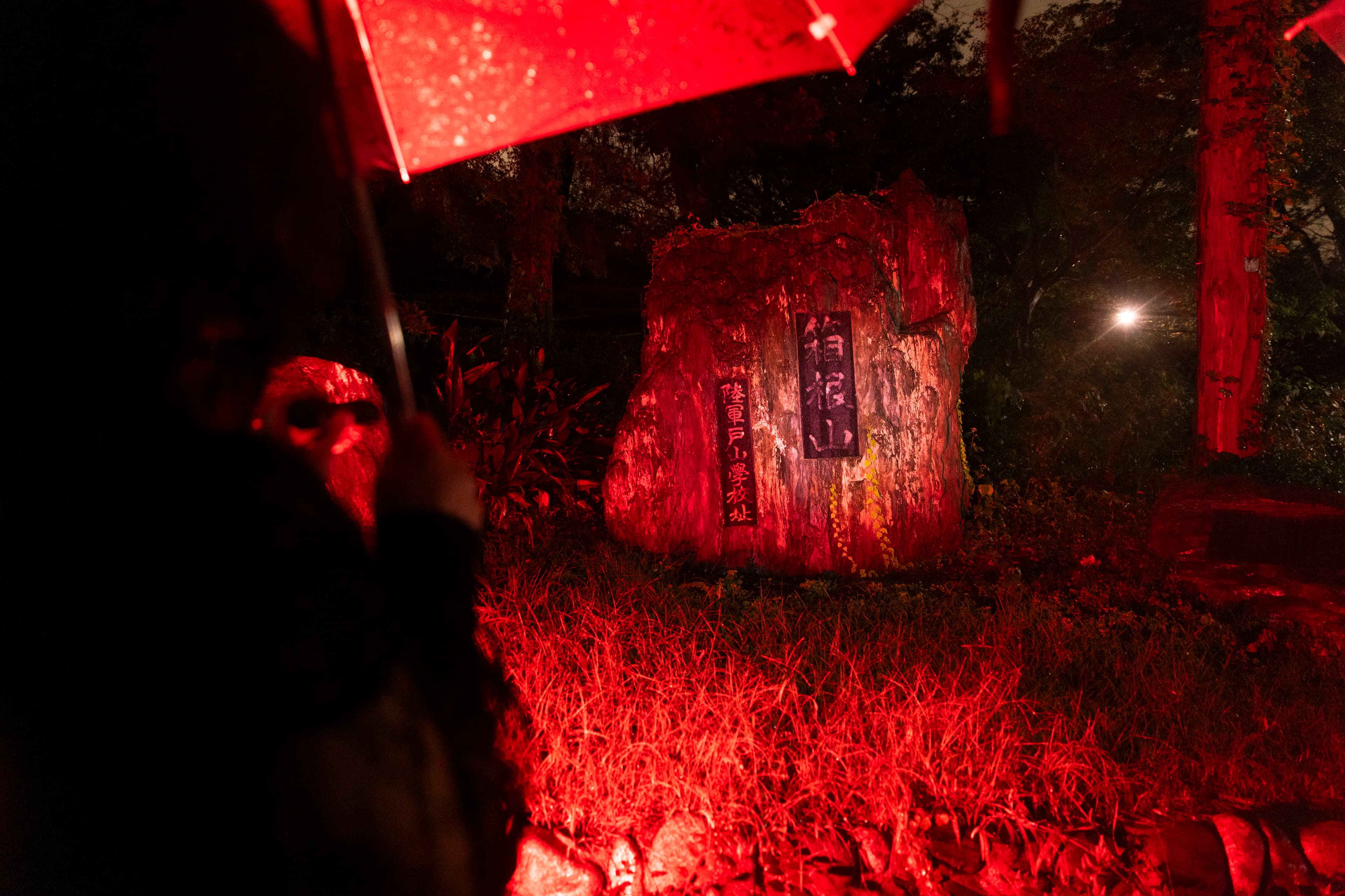 A stone monument bathed in red light on a rainy night